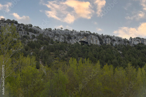 Landscape of a rocky mountain with caves surrounded by trees of a forest in a sunny sunset