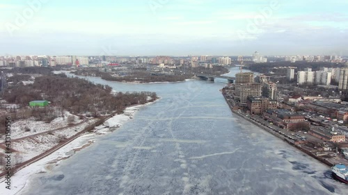 Aerial video: flies over a frozen river in winter towards the automobile bridge, in the frame of a house under construction on the bank