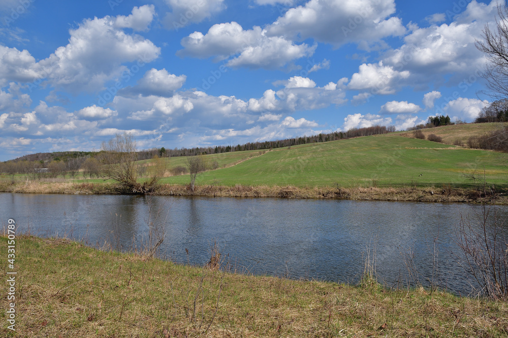 Peacefull river Massawippi during spring season with field background and blue sky filled with white clouds. Wondefull countryside