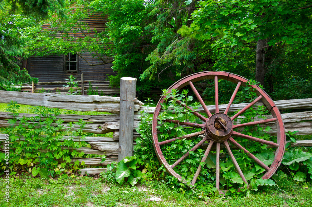 Wood spoke wagon wheel left on the wooden fence on a farmhouse Wood spoke wagon wheel left on the wooden fence on a farmhouse