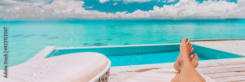 Luxury vacation swimming pool banner background. Woman lying down relaxing on lounger sunbathing legs and feet in summer sun. Travel holiday panoramic.