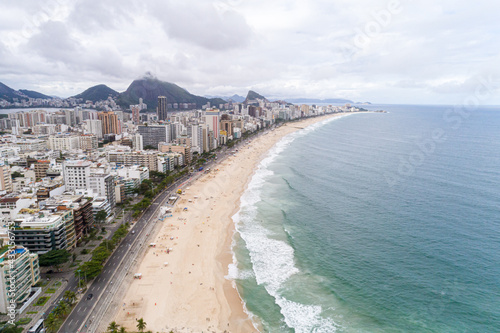 Vista aérea da praia do Leblon e Ipanema, com lindo mar verde, faixa de areia com pouca gente, avenida à beira-mar com seus prédios residenciais.