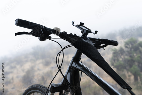 Black bicycle handlebars with cellphone holder and mountains on blurred background on foggy day. Sport adventure concept