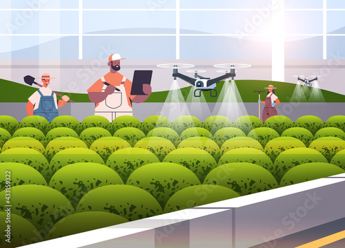 farmers controlling agricultural drones sprayers quad copters flying to spray chemical fertilizers in greenhouse