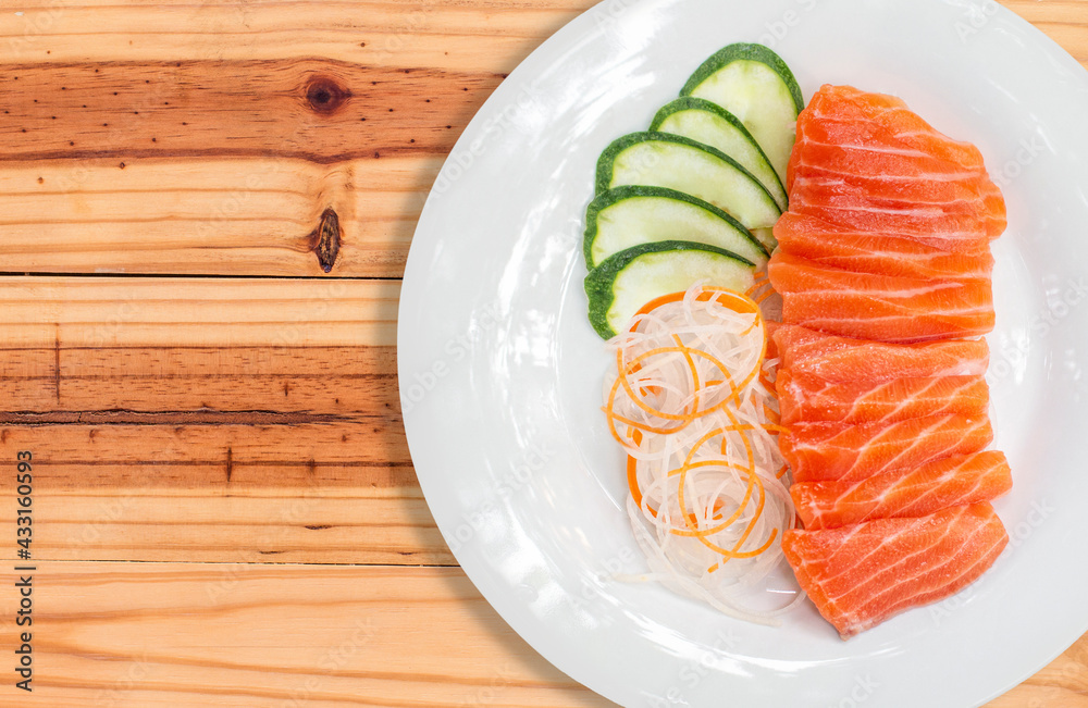 raw salmon red fish and vegetables on white plate with wooden background raw salmon red fish and vegetables on white plate with wooden background