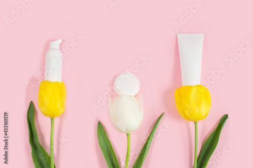 White cosmetic bottles containers on yelolow and white tulips flowers. photo