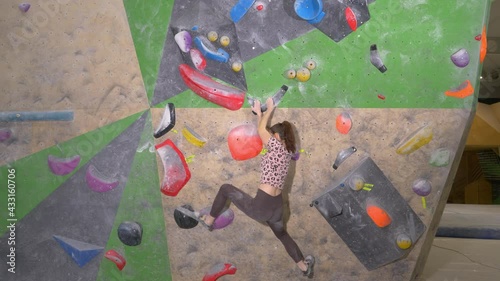 CLOSE UP: Unrecognizable nimble woman climbs up an indoor bouldering route. Fit Caucasian female athlete trains at an indoor climbing facility. Cinematic shot of a strong woman rock-climbing indoors.