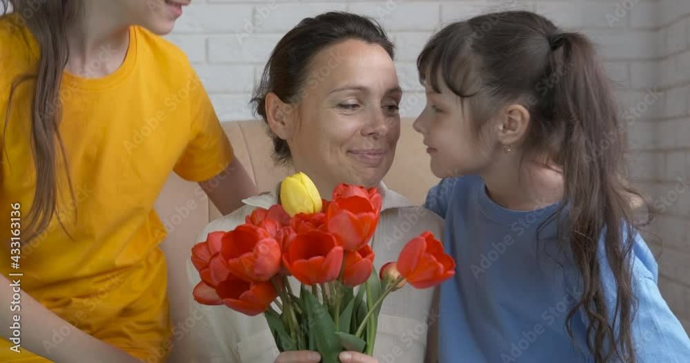 Mother birthday with flowers and daughters. Two happy daughter embrace her mother with flowers and celebrate a mother's day. Mother's Day. Mother birthday with flowers and daughters. Two happy daughter embrace her mother with flowers and celebrate a mother's day. Mother's Day.