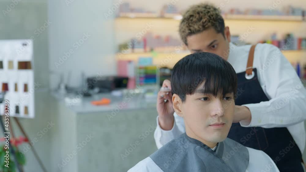 A professional barber Asian man uses scissors and combs to trim hairs for customers in his barber shop. Barber shop and haircut concept A professional barber Asian man uses scissors and combs to trim hairs for customers in his barber shop. Barber shop and haircut concept