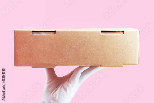 Female hand in glove holds cardboard box, food delivery concept.