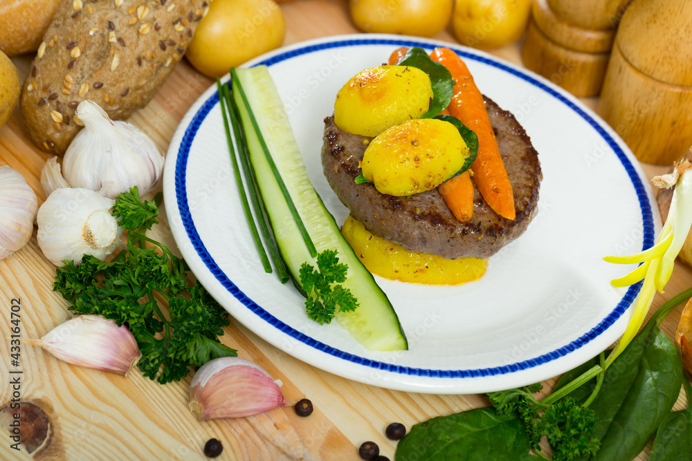 Delicious beef rissole with garnish of roasted new potatoes, baked carrots, cucumber and greens