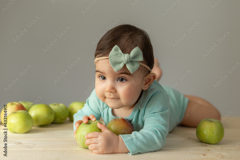 portrait of a little girl in a green bodysuit on a wooden table with fresh green apples. Natural products for children. High quality photo