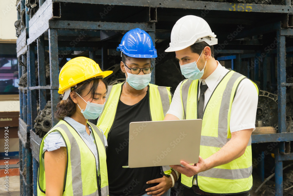 Men and woman work together, wear safety facemask and using laptop. Black women looking at screen on laptop while Caucasian engineer men discuss with Asian engineer women in factory-warehouse Men and woman work together, wear safety facemask and using laptop. Black women looking at screen on laptop while Caucasian engineer men discuss with Asian engineer women in factory-warehouse