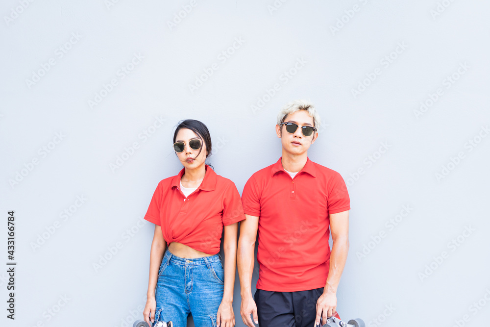 Half body of Asian handsome man and cute woman stand on center, place skateboards in vertical, looking straight, and act smart at cool wall with copy space in daylight time, summer holiday Half body of Asian handsome man and cute woman stand on center, place skateboards in vertical, looking straight, and act smart at cool wall with copy space in daylight time, summer holiday