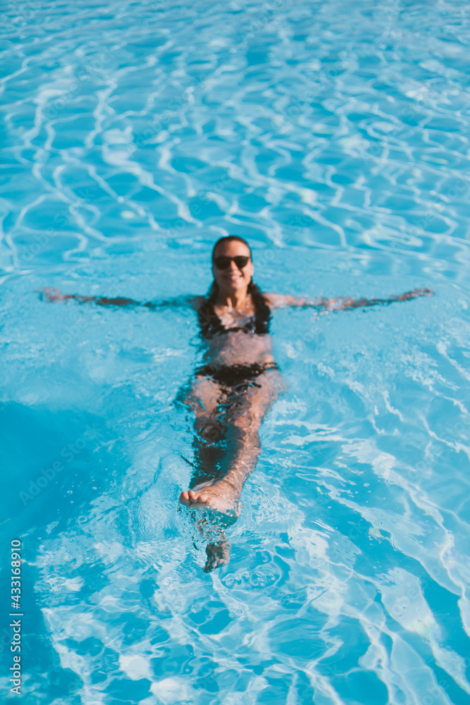 Girl swimming in luxury pool with her back. Relaxing time and healthy leisure activities in summer.