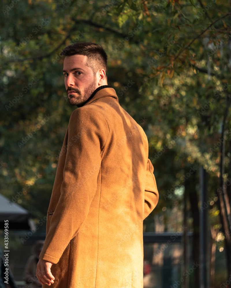 Fototapeta premium Fall portrait of a bearded man with a brown coat at sunset time in the park