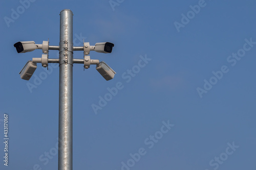 Low angle view of the surveillance security cameras on steel pole in outdoor public car parking with clear blue sky background.
