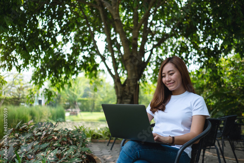 A young asian woman working and typing on laptop keyboard while sitting in the park