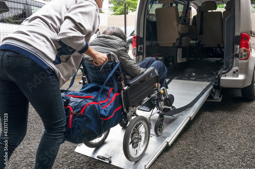 デイサービスの送迎車に乗せられる高齢者の女性。 An elderly woman in a car to go to a day care facility.	