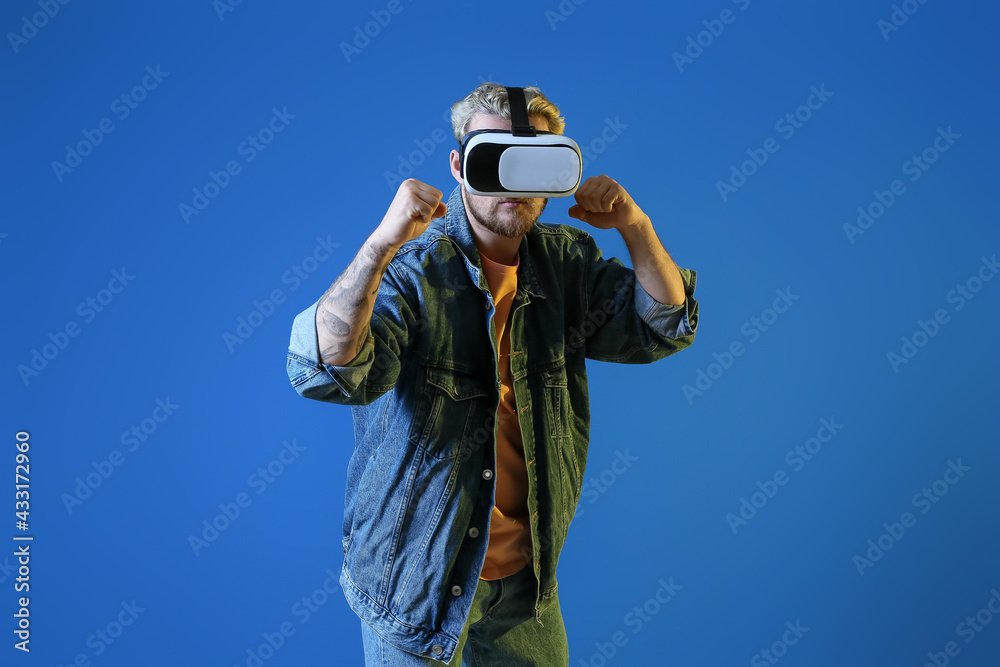 Young man with VR glasses on color background