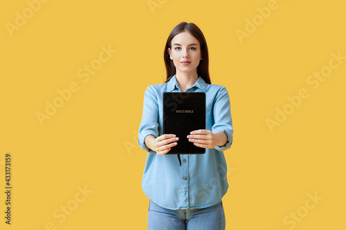 Young woman with Bible on color background photo