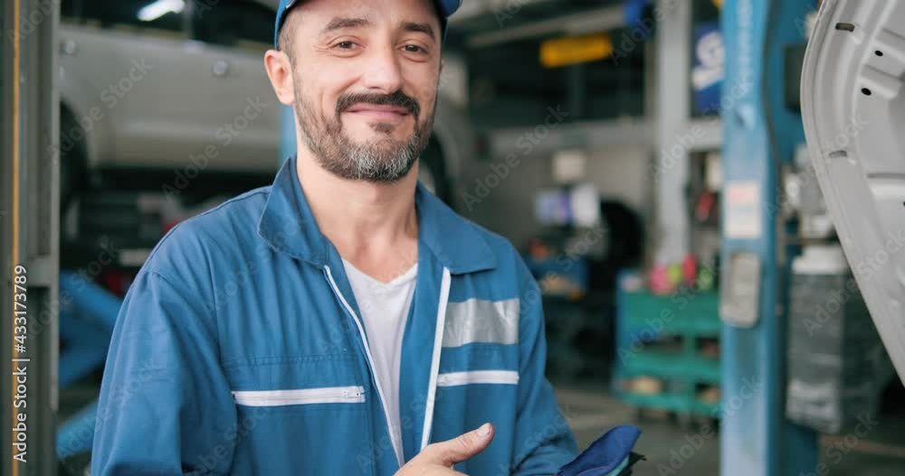 Smiling car mechanic standing look at camera in garage, Portrait of Caucasian man technician master in uniform in front of automobile. Repairing car service concept