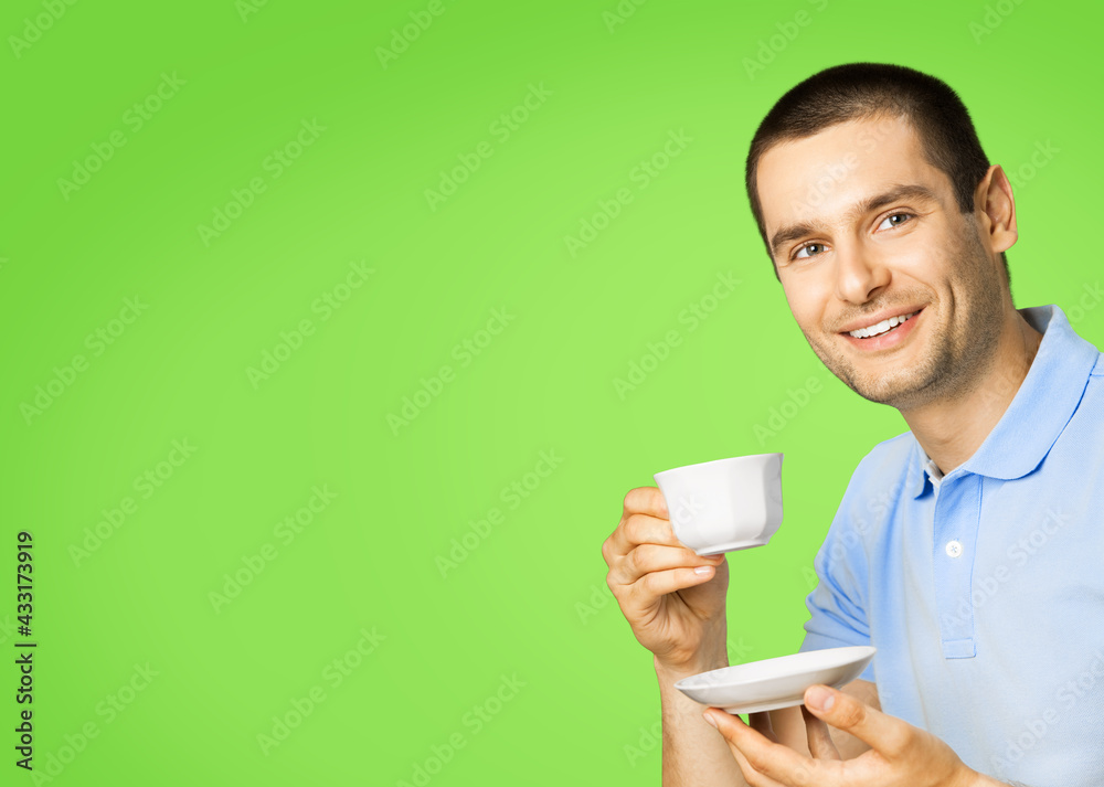 Portrait of young happy smiling man in blue casual clothing drinking coffee, isolated over green color background. Portrait of young happy smiling man in blue casual clothing drinking coffee, isolated over green color background.