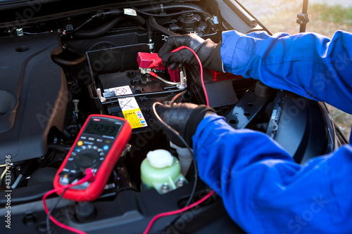 Fotografie Technician uses multimeter voltmeter to check voltage level in car battery