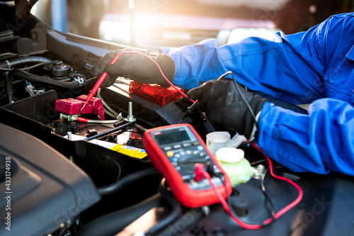 Technician uses multimeter voltmeter to check voltage level in car battery. Service and Maintenance car battery.