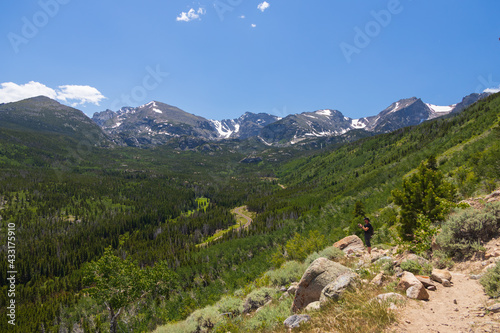 Hiker on Bierstadt Lake Trail with blue sky and mountains in background in Rocky Mountain National Park, Colorado  © Martina