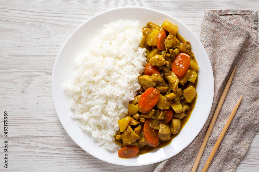 Homemade Japanese Chicken Curry on a white plate on a white wooden surface, top view. Flat lay, overhead, from above. Homemade Japanese Chicken Curry on a white plate on a white wooden surface, top view. Flat lay, overhead, from above.
