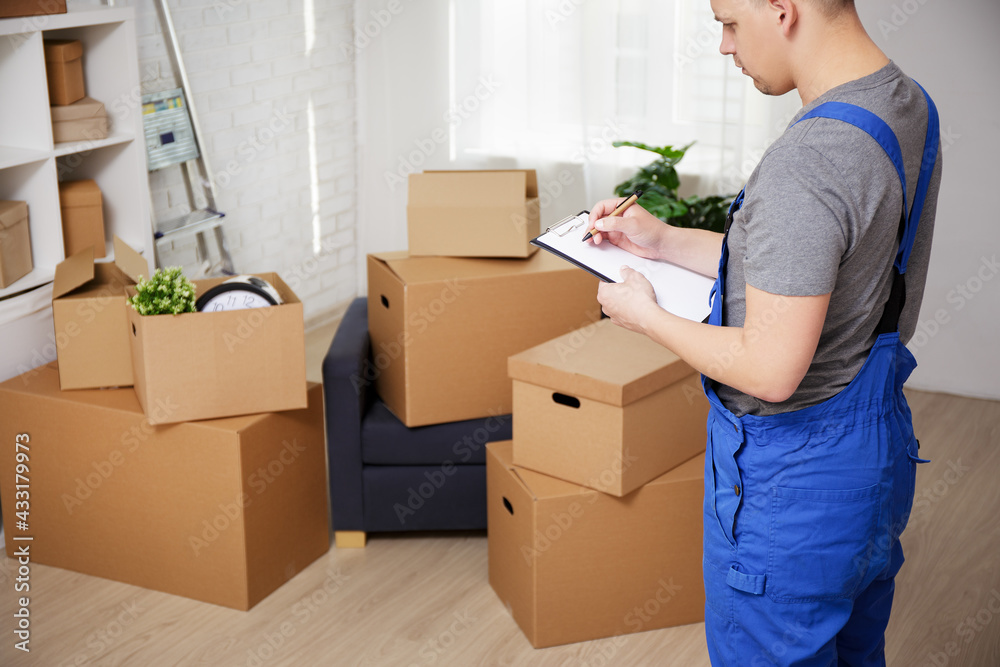 moving day concept - loader looking on cardboard boxes and writing something on clipboard. moving day concept - loader looking on cardboard boxes and writing something on clipboard.
