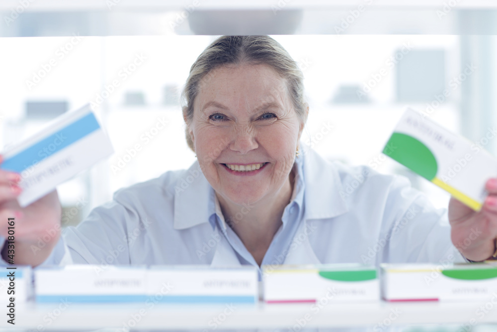 Pharmacist is working. Woman wearing special medical uniform. A woman looks through apathetic shelves and shows a package of medicines