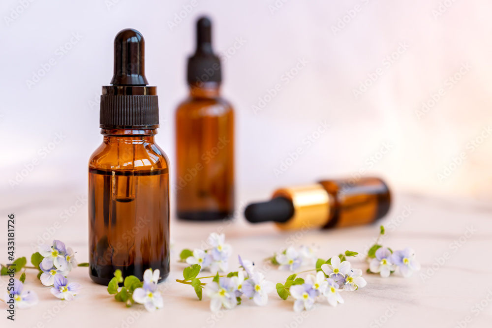 Fototapeta premium set of different bottles with beauty serum, hyaluronic acid and vitamins on light background with wild flowers. Home spa concept