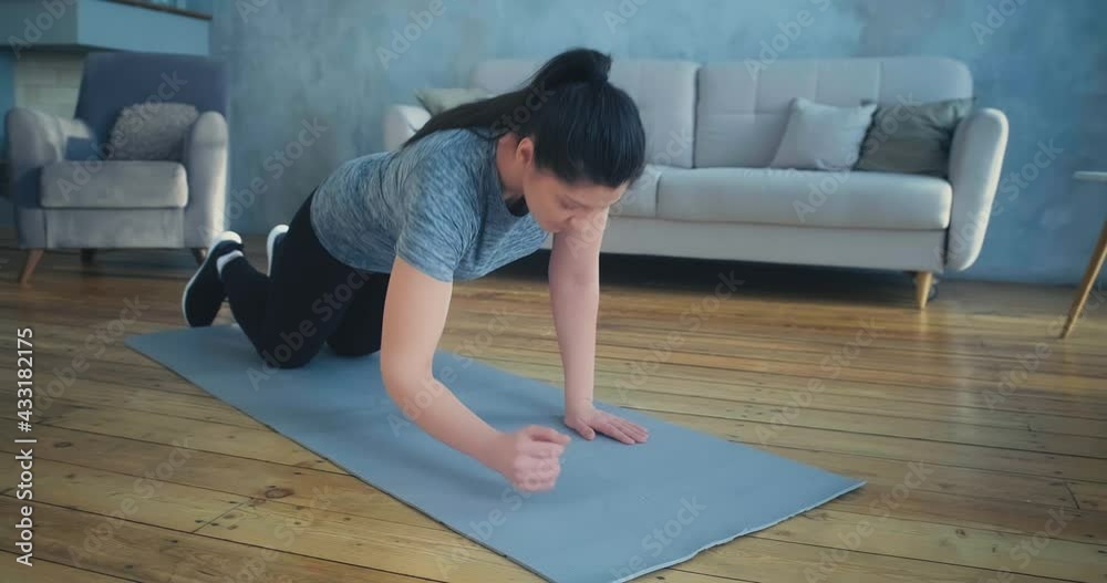 sportive woman does plank exercise on grey mat near sofa in spacious living room slow motion