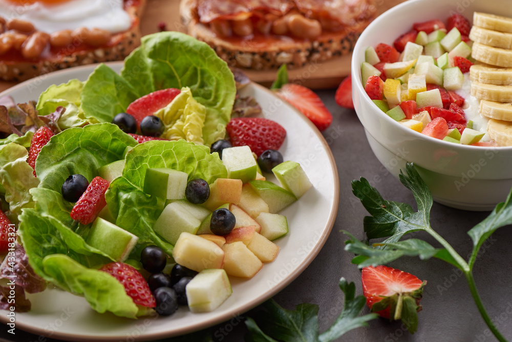 variety of open sandwiches made of brown whole wheat bread with tomatoes sauce, bowl of oat granola with yogurt, white beans, bacon, fried egg. fresh fruit and vegetable salad, healthy breakfast. variety of open sandwiches made of brown whole wheat bread with tomatoes sauce, bowl of oat granola with yogurt, white beans, bacon, fried egg. fresh fruit and vegetable salad, healthy breakfast.