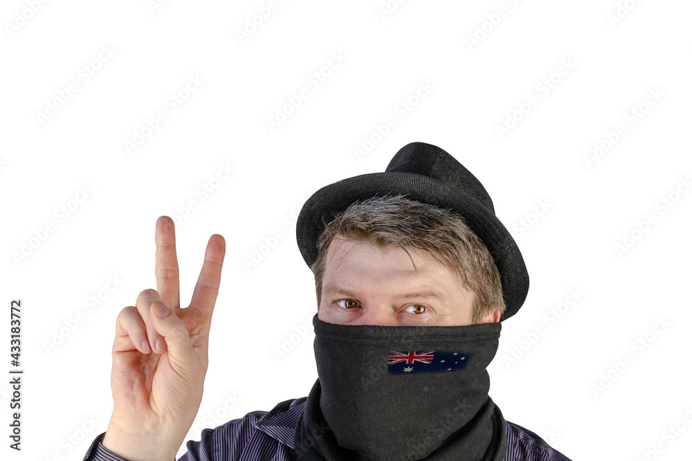 Adult man in a black hat with small fields and a scarf over his face shows a victory gesture.