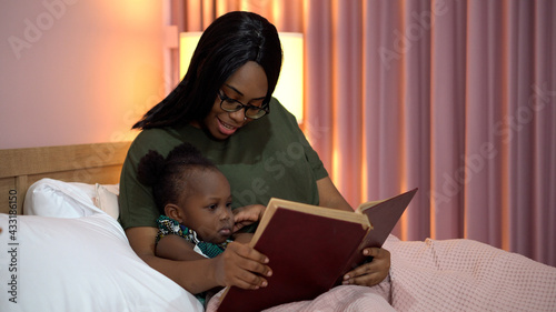 Fotografie african american mother reading a book to her little daughter in bed before going to sleep at home