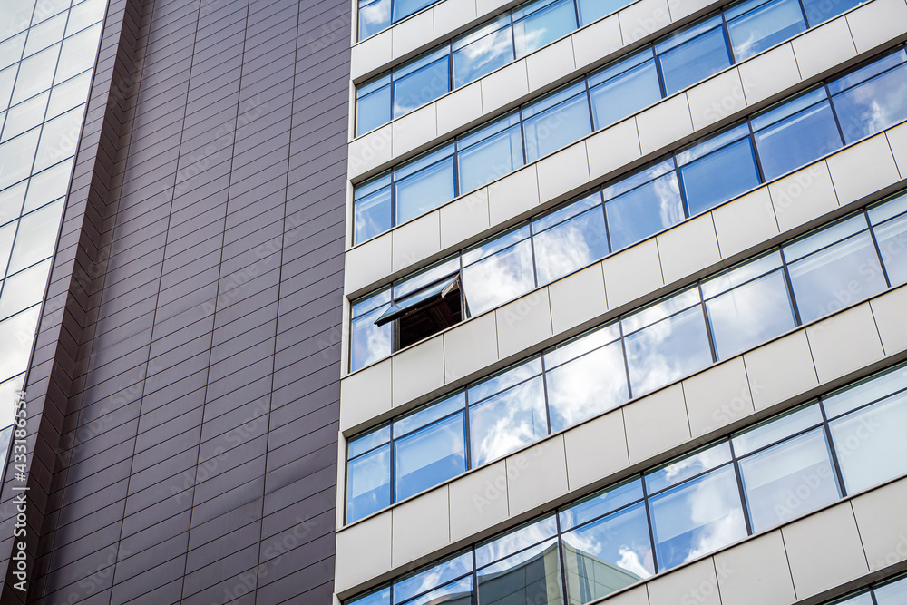 Modern facade of office building with glass and steel. One open window. Reflection sky and clouds. Exterior of futuristic business building.