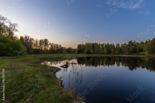 Spring landscape, river, bushes and trees, reflected in the water. Sunset sky. Bright spring greenery in the landscape.