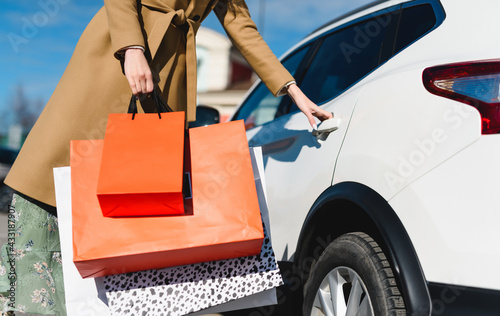 Successful shopping! A woman shopaholic opening the car door to load a lot of packages from different stores