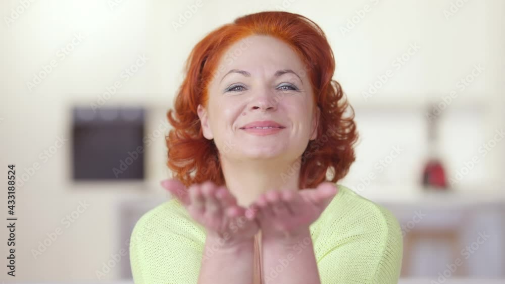 Charming beautiful positive woman showing heart gesture and sending air kiss looking at camera. Portrait of happy Caucasian redhead lady posing indoors at home. Joy and lifestyle Charming beautiful positive woman showing heart gesture and sending air kiss looking at camera. Portrait of happy Caucasian redhead lady posing indoors at home. Joy and lifestyle