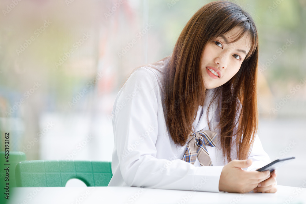 Asian young woman student holding hand smartphone in smart and happy pose at college. Teenage education with technology learning girl in school uniform. Asian young woman student holding hand smartphone in smart and happy pose at college. Teenage education with technology learning girl in school uniform.