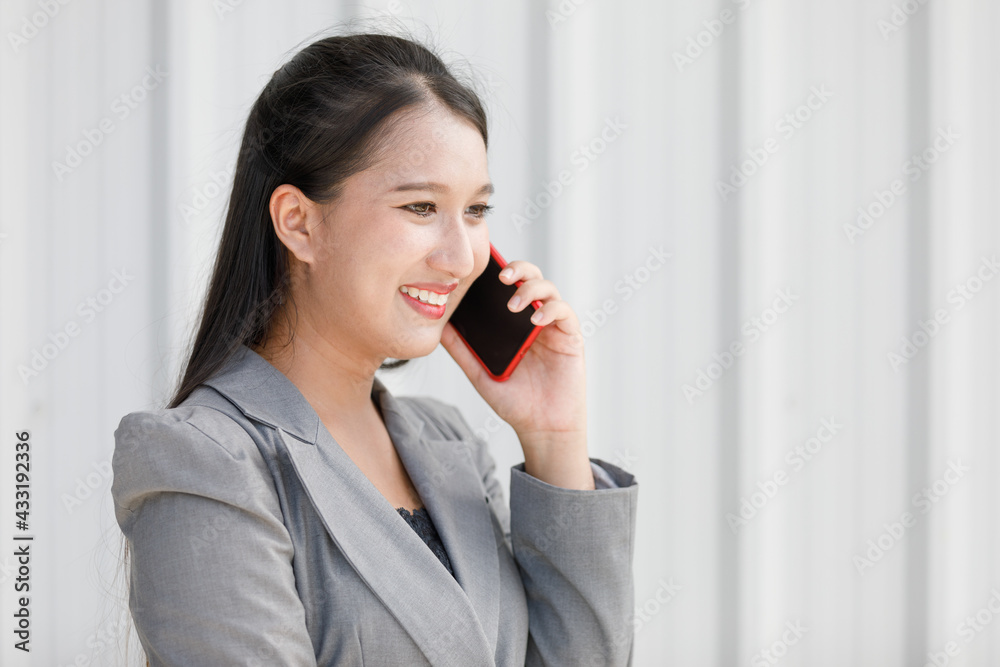Asian smiling woman holding hand smartphone. Businesswoman talk about work over the phone in office room. Concept Beautiful and confident working woman. Asian smiling woman holding hand smartphone. Businesswoman talk about work over the phone in office room. Concept Beautiful and confident working woman.