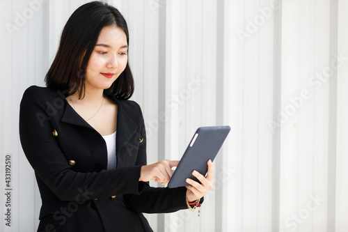 Asian plump woman standing wearing black suit. Businesswoman holding hand tablet to working in office room and white background. Concept beautifull lady confident.