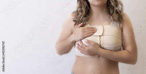 Young woman in beige compression bra bandage after breast augmentation surgery mammoplasty. banner. advertising. copy space