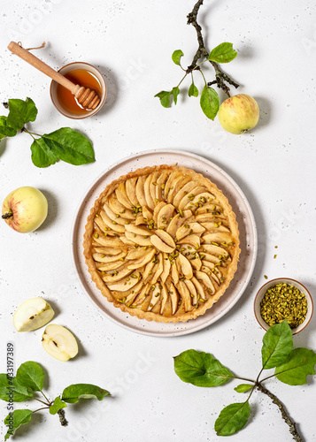 Top view of freshly baked apple pie tart with custard filling and green pistachios on a light stone background. Healthy homemade food concept.