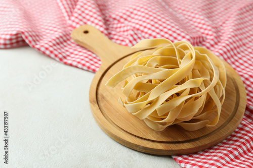 Board with uncooked pasta and kitchen towel on white textured background
