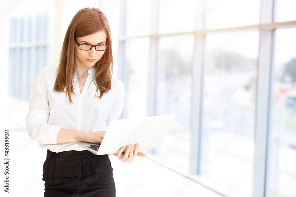Beautiful female specialist with laptop computer standing in sunny office and smiling charmingly. Business people concept Beautiful female specialist with laptop computer standing in sunny office and smiling charmingly. Business people concept