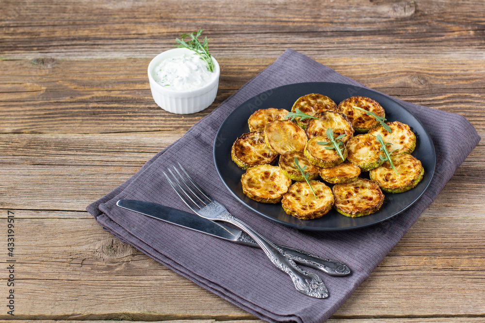 Fried slices of zucchini with sour cream sauce. Courgettes with herb for dinner on natural wooden background Fried slices of zucchini with sour cream sauce. Courgettes with herb for dinner on natural wooden background